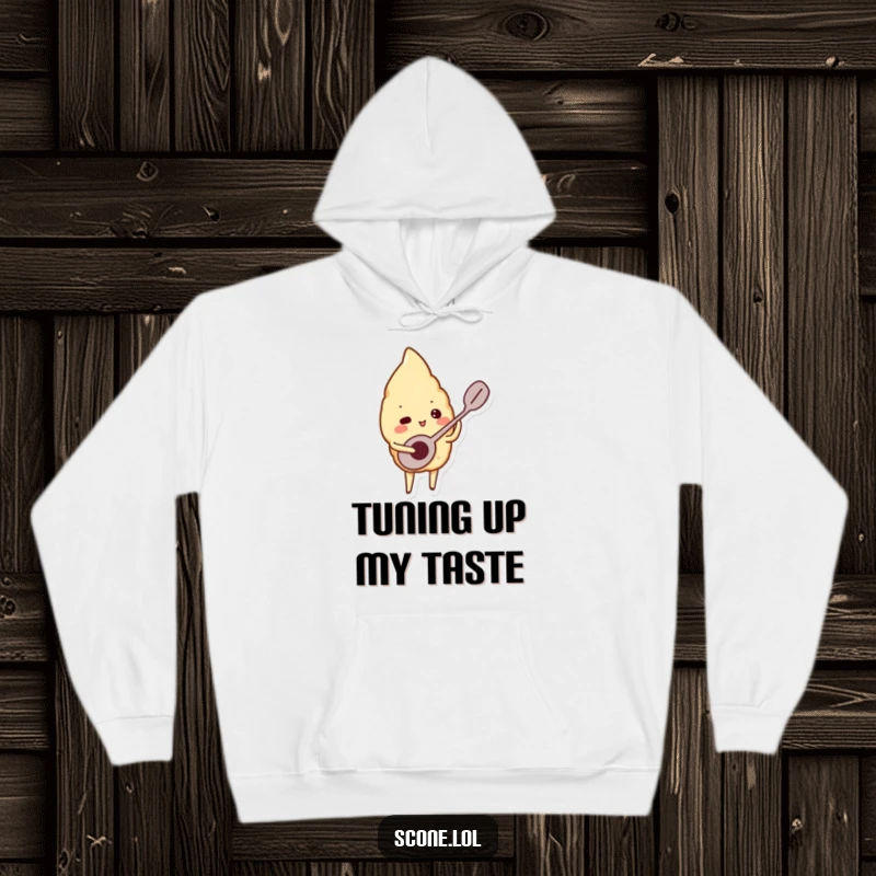 Funny hoodie featuring a scone character playing a tiny spoon like a musical instrument, offering cozy comfort and cheerful vibes.